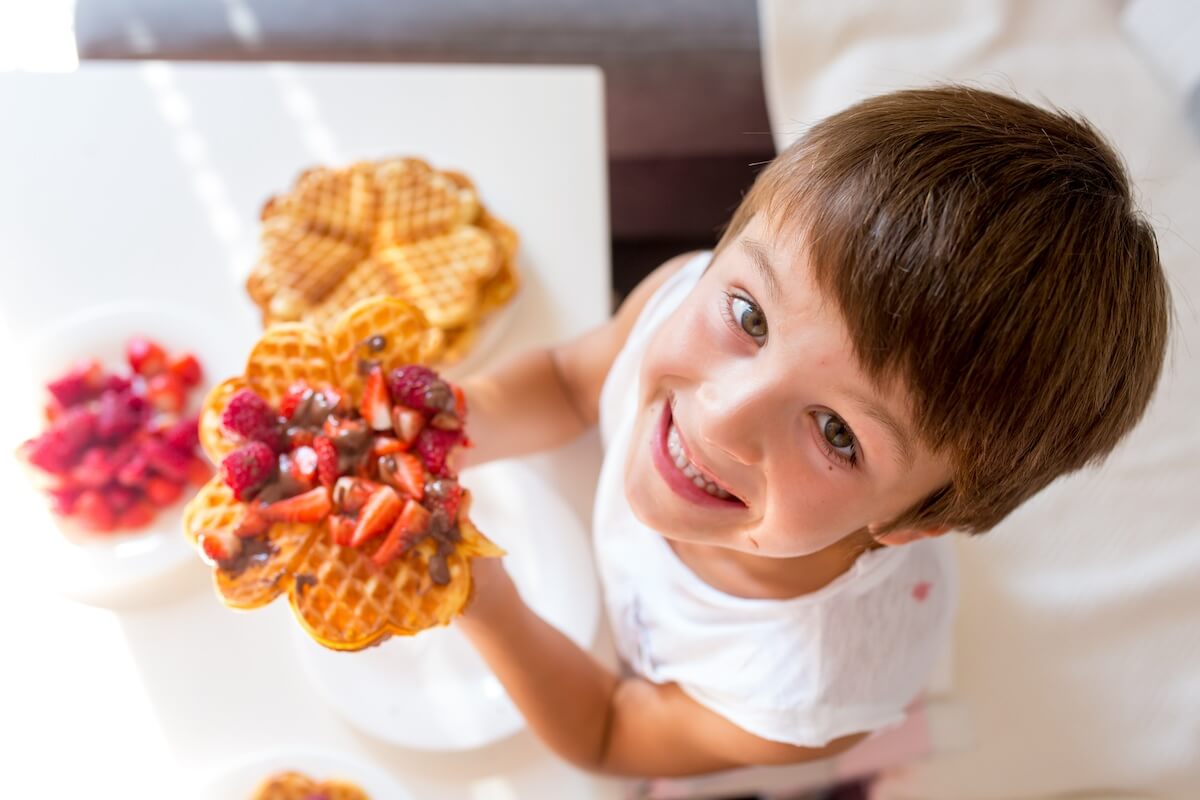 happy little boy looking up at camera with a huge stack of waffles and berries.
