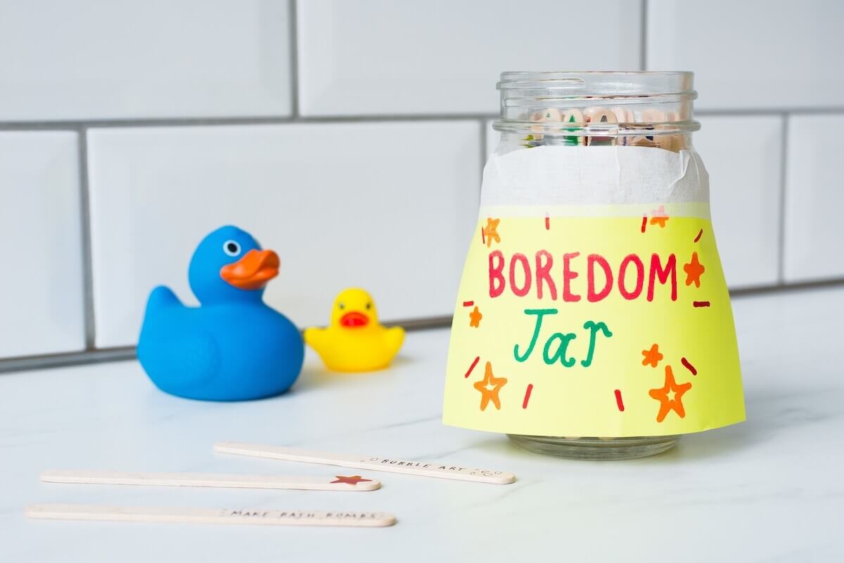 boredom jar sitting on a white benchtop with 2 rubber ducks nearby