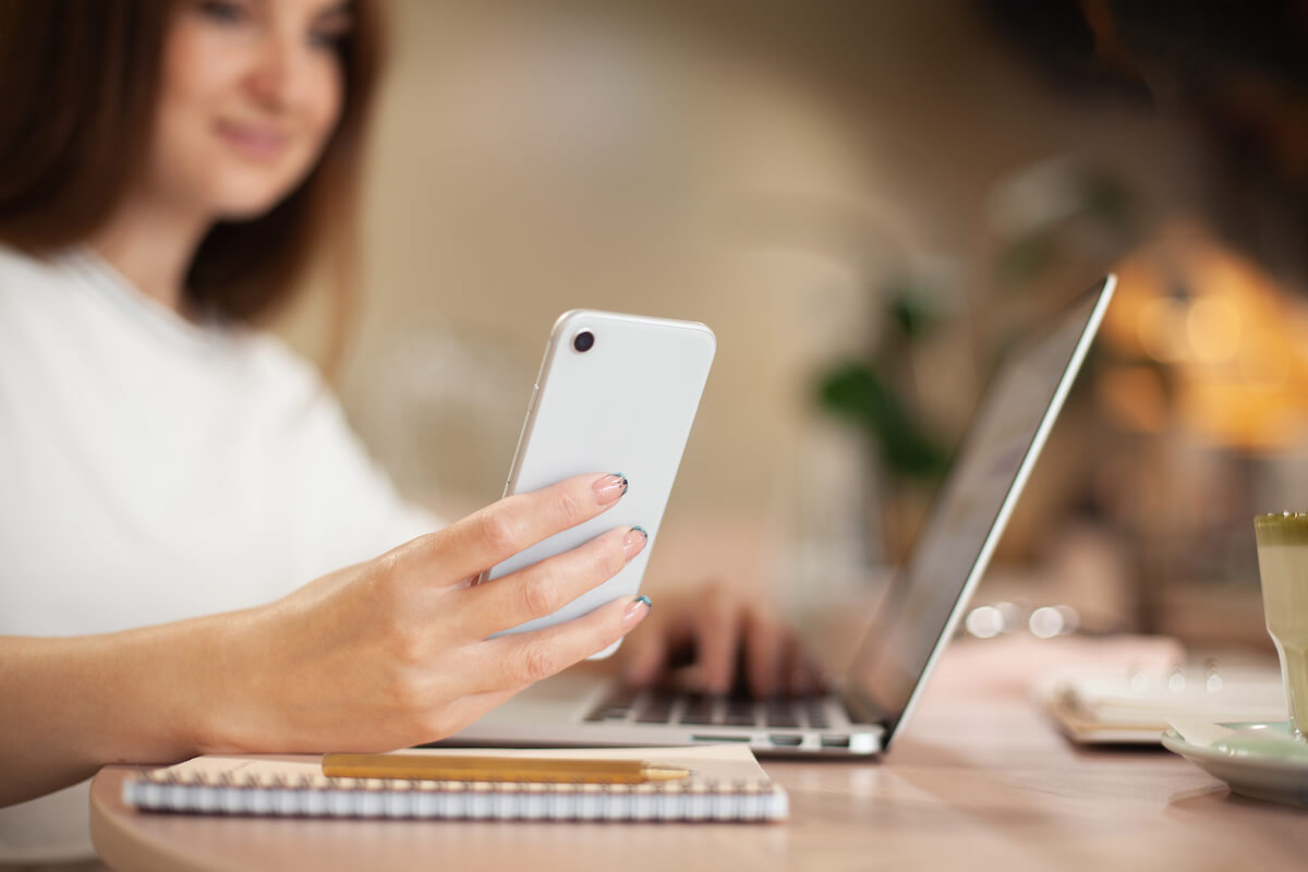 woman sitting at her desk with her laptop open and looking at her phone