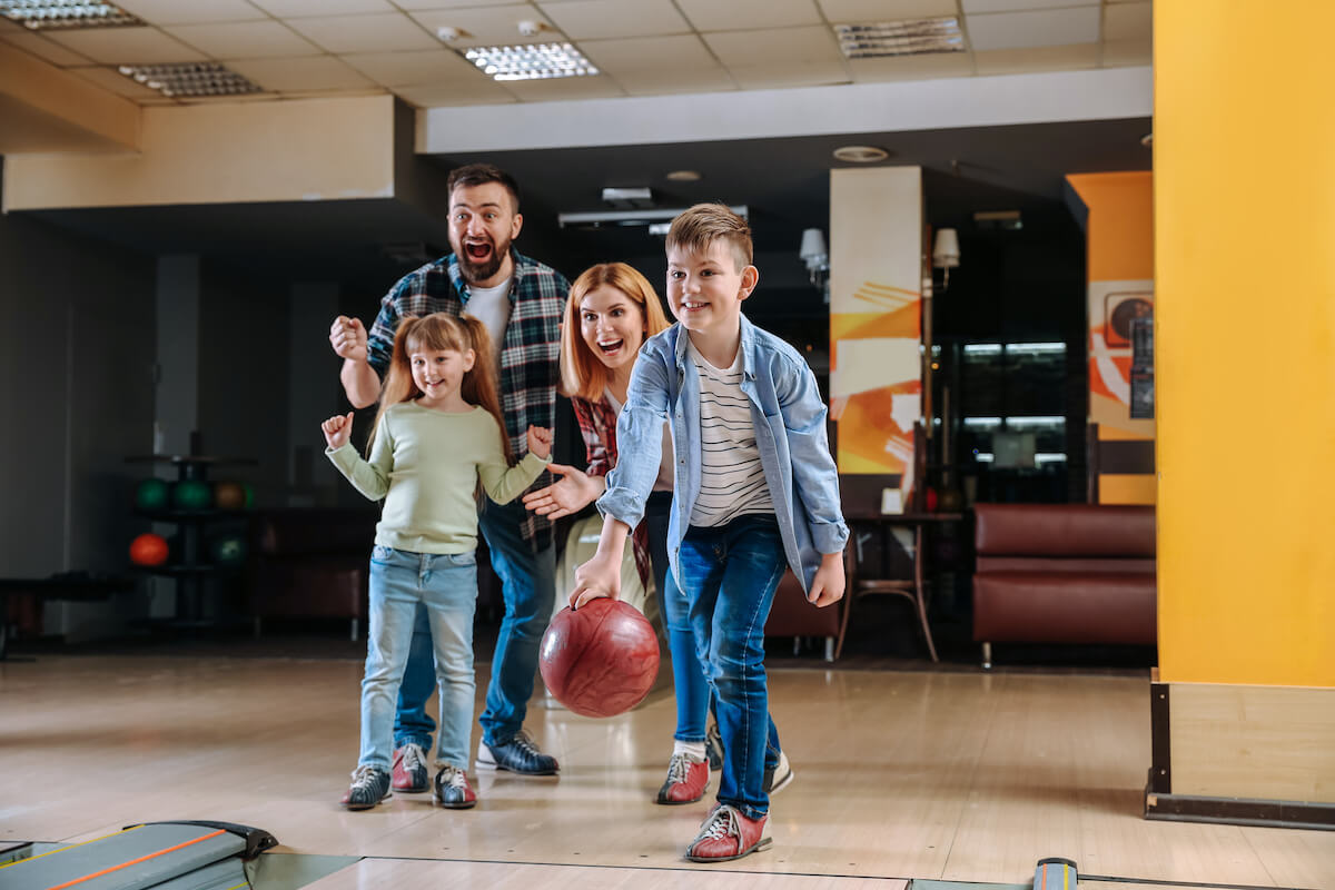 family with two kids at the bowling alley cheering on a little boy as he bowls a red ball