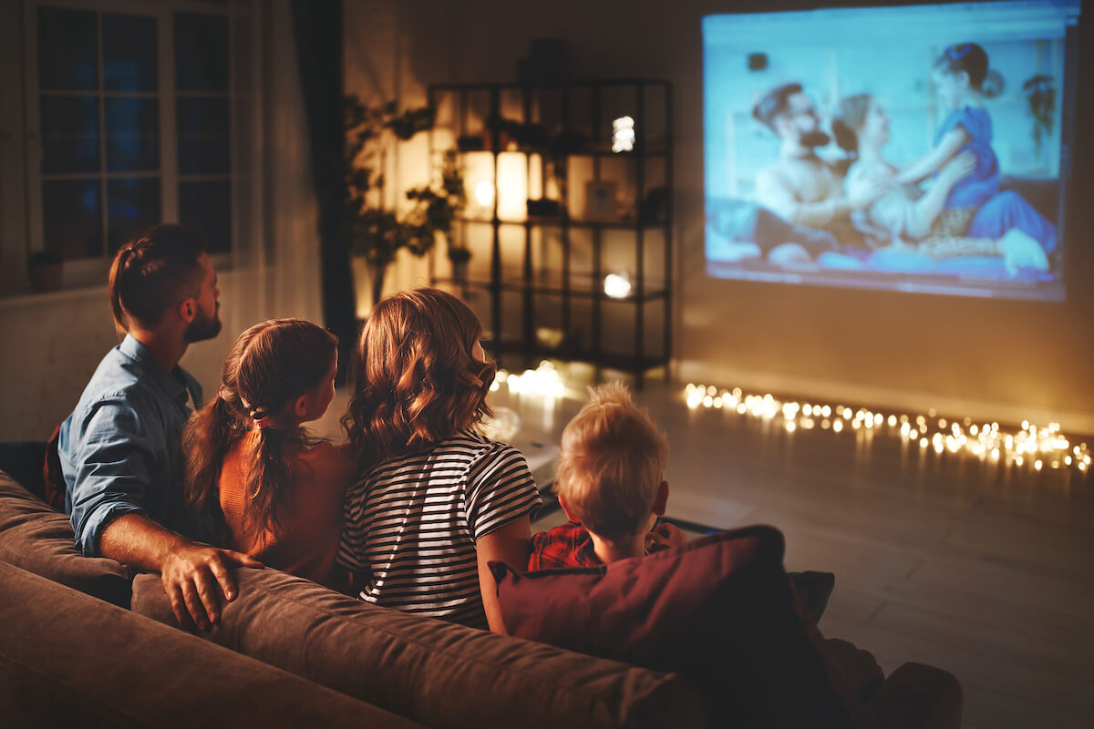 family of 4 sitting on their couch with fairy lights on, watching a movie at home