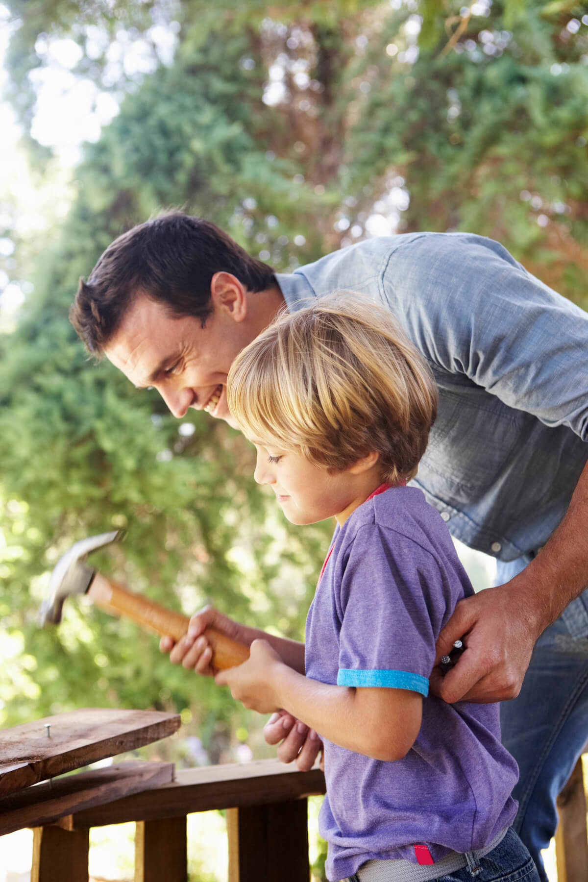 Father teaching son to hammer a nail while building a tree house