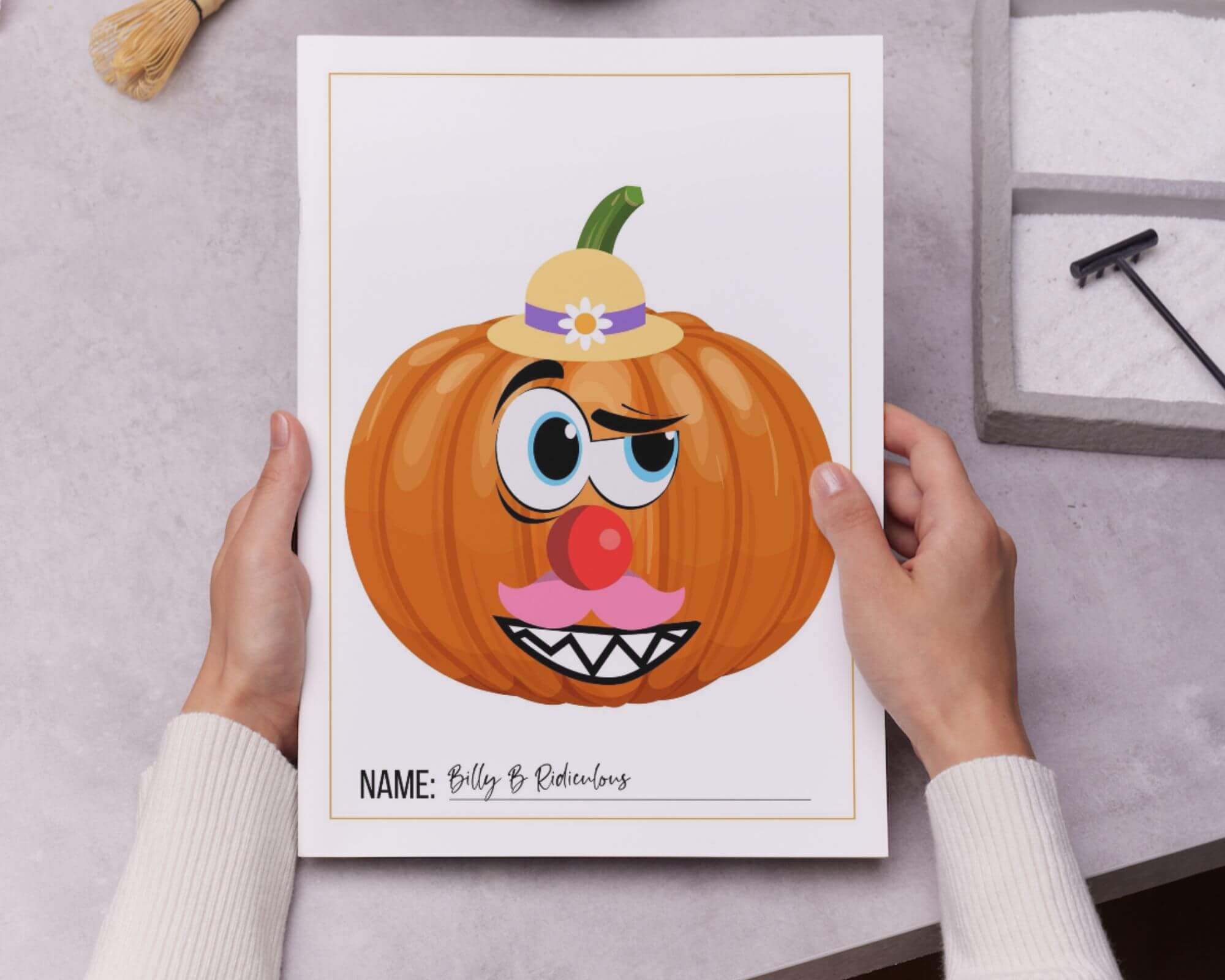 Image of a person holding a piece of paper with a printed pumpkin that has funny facial features stuck on. 