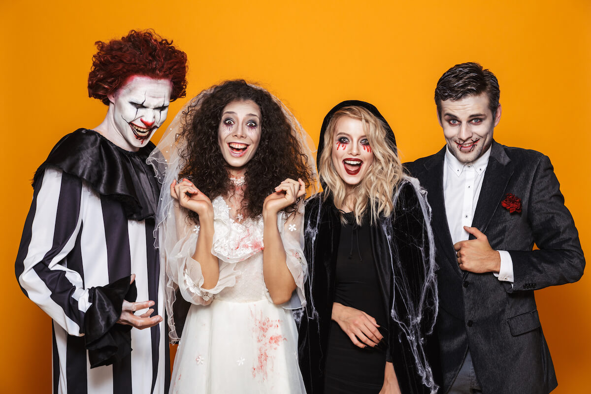 four people dressed up in halloween costumes including a clown, bride, witch and vampire with an orange background