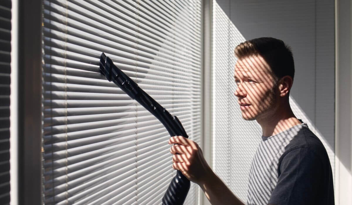 man vacuuming vertical blinds on window