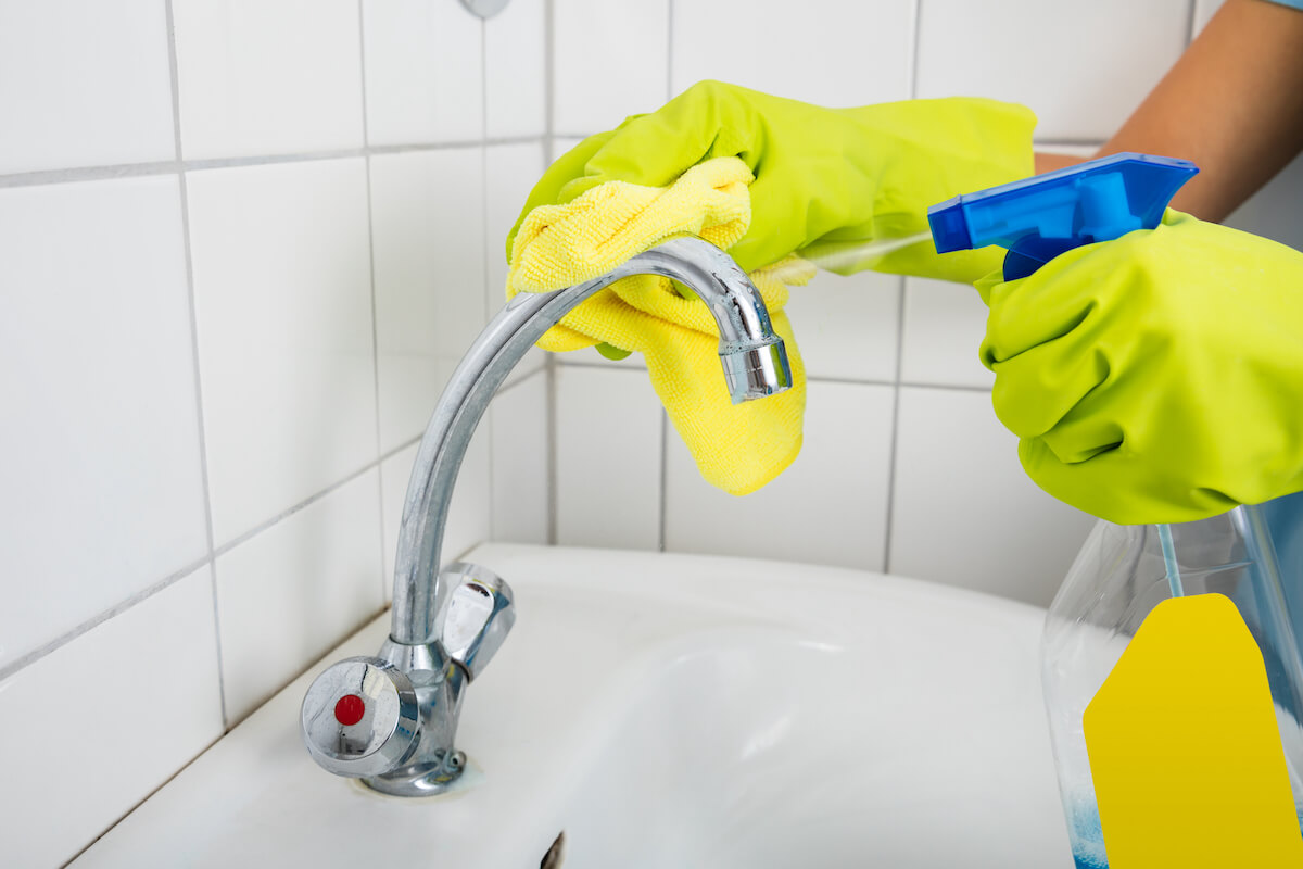 person spraying and cleaning a bathroom tap