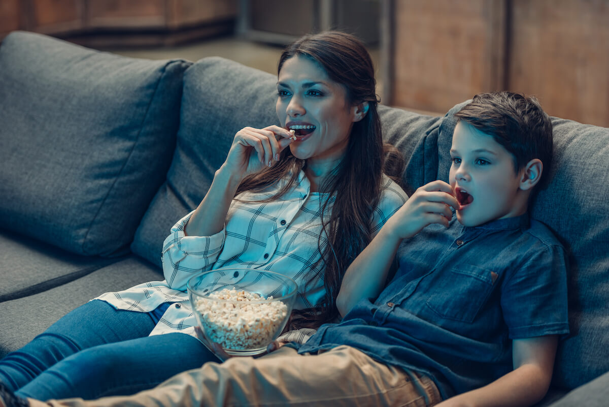 mother and son on couch watching a movie and eating popcorn