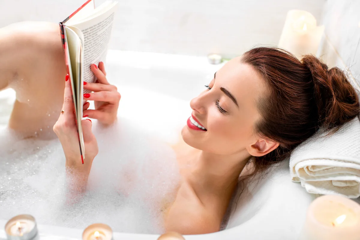 woman relaxing in a bubble bath with a book and candles