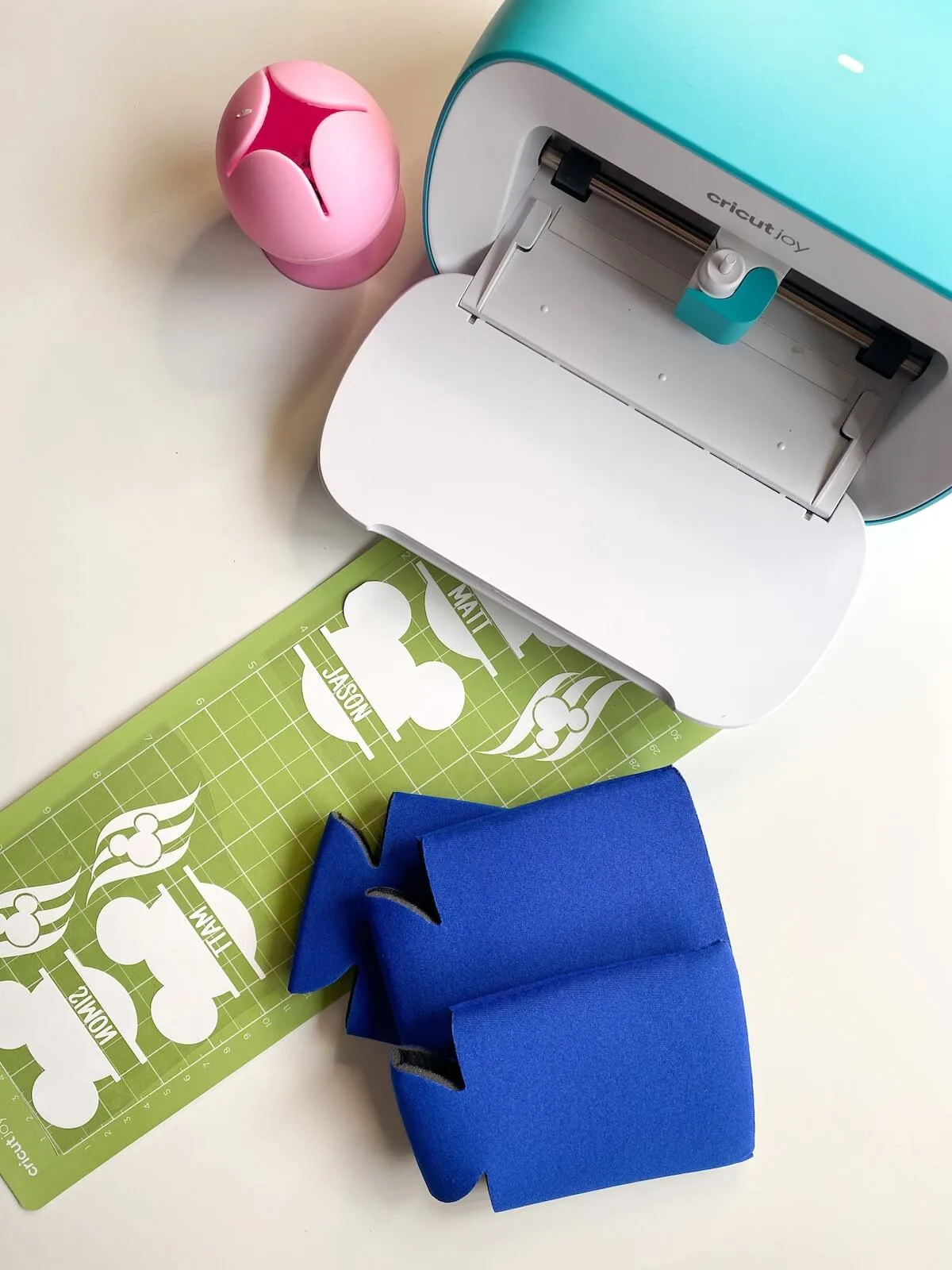 cricut joy with vinyl cut on mat and blank can koozies.