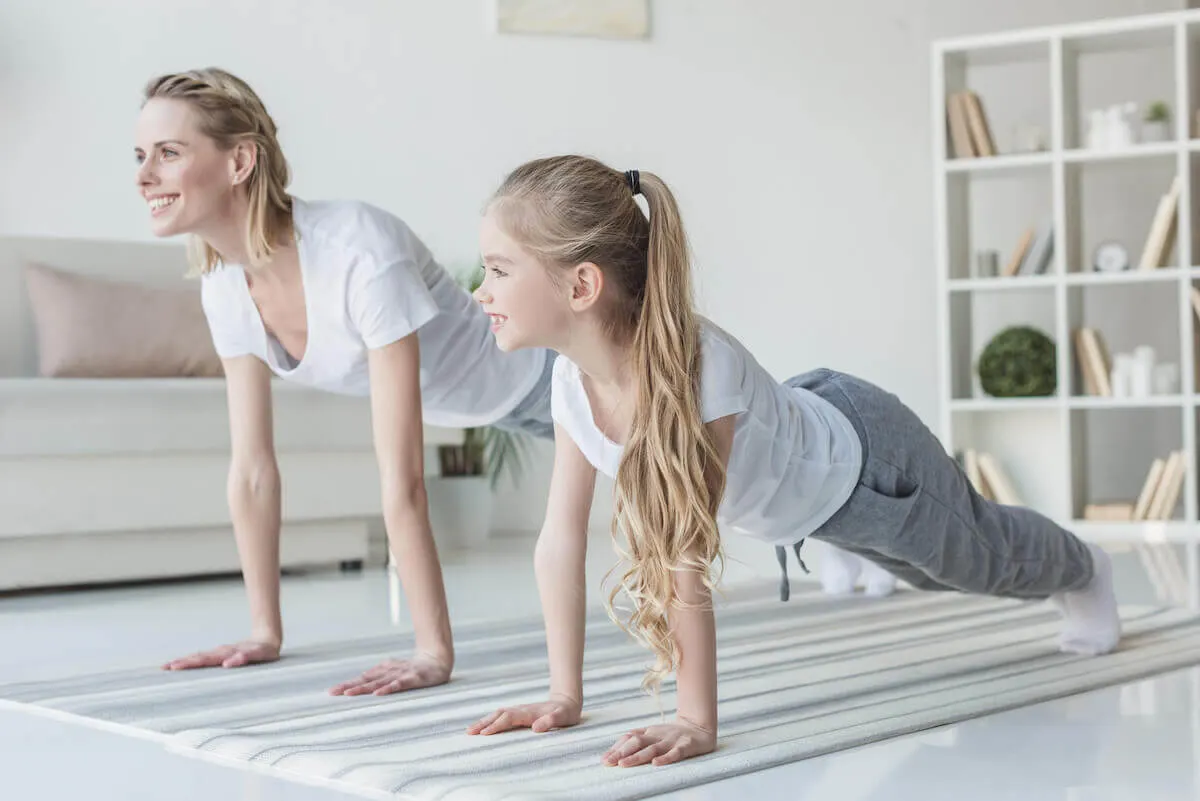 mother and tween daughter doing yoga stretches in a large living room, wearing white tshirts and trackpants